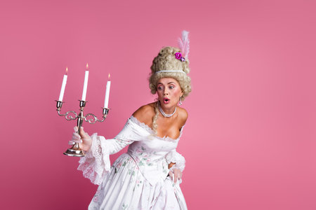 Sophisticated young woman in vintage baroque attire holding a candelabrum with a playful expression...