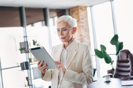 Mature elegant businesswoman in a modern office workspace using a digital tablet, conveying professionalism and successの写真素材