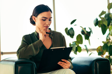 Young professional businesswoman reviewing documents in modern office workspace, representing confidence and professionalismの写真素材