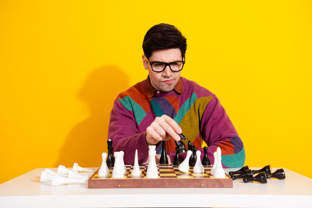 Young man concentrating on a chess move in a retro sweater against a bright yellow background.の写真素材