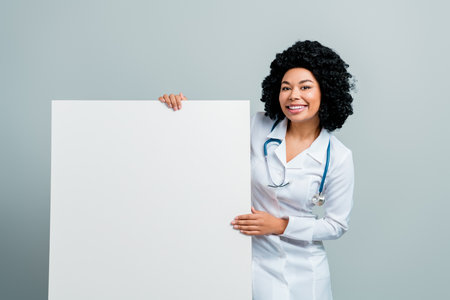 Confident female doctor holding a blank board in medical uniform with a stethoscope, smiling in a healthcare settingの写真素材