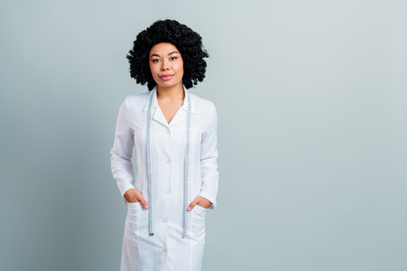 Confident female professional in white coat with measuring tape, standing against a gray background, exuding expertiseの写真素材