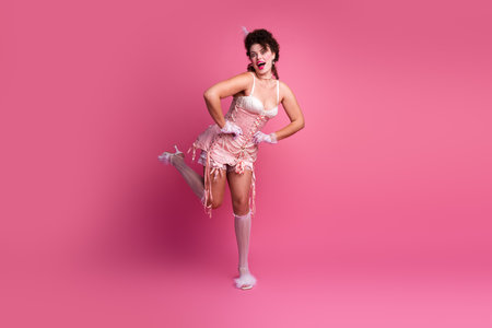 A young woman in a playful pose, dressed in an elegant pink costume against a vibrant pink backgroundの写真素材