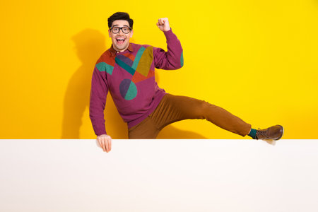 Cheerful young man posing against a bright yellow background, showcasing style and personality with...