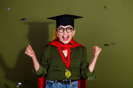 Excited female graduate celebrating achievement with a medal and confetti on a bright green backgroundの写真素材