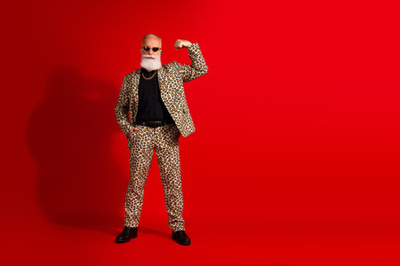 Senior man in leopard print suit striking a pose against a vibrant red backgroundの写真素材