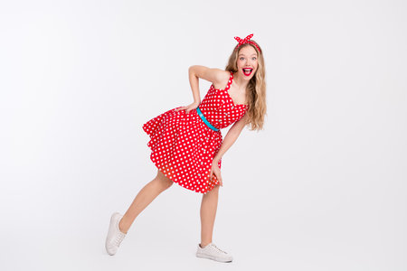 Cheerful woman in polka dot retro dress dancing on white background showing lively style and playful energyの写真素材