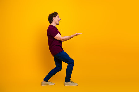 Young man in burgundy polo shirt making a hand gesture against a yellow background, expressing excitement and energyの写真素材