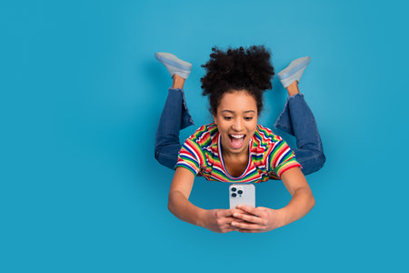 Young woman with curly hair using a smartphone while smiling and enjoying leisure time against a...