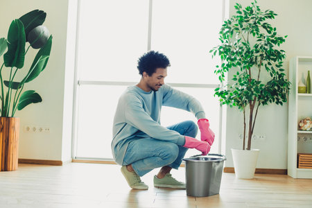 Young man wearing casual clothes cleaning and tidying a modern living room with houseplants during the weekend on a relaxing dayの写真素材