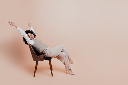 Young professional businesswoman in formal attire stretching and relaxing on a beige background during a moment of restの写真素材