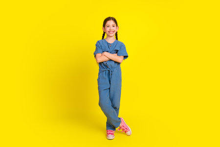 Smiling young girl in casual blue attire standing confidently on vibrant yellow background with...