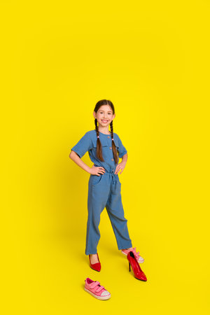 Young girl standing confidently in blue casual attire with playful poses against a bright yellow backgroundの写真素材