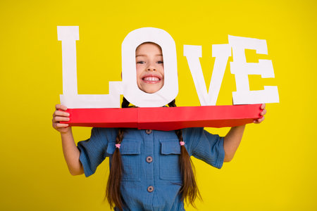 Happy young girl holding a red tray with the word love on yellow backgroundの写真素材