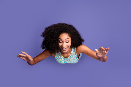Joyful young woman celebrating freedom with raised hands on vibrant purple backdrop, embodying...