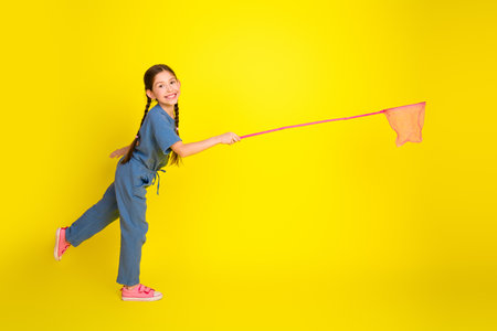 Joyful young girl with braided hair playing with a net against vibrant yellow background in stylish casual outfitの写真素材