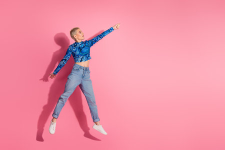 Energetic young woman wearing stylish blue top and jeans posing against a vibrant pink background with a confident raised handの写真素材