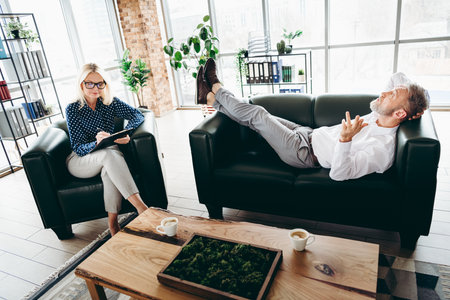 Professional counseling session in modern office environment with a mature businessman sharing thoughts and a businesswoman taking notes.の写真素材