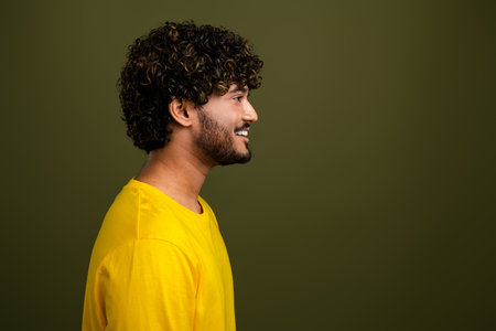 Portrait of a cheerful young man in a yellow shirt against a khaki background showcasing modern casual style with curlsの写真素材