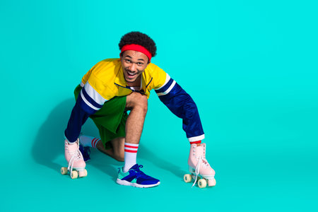 Young man wearing retro sportswear crouching with roller skates on a bright turquoise background