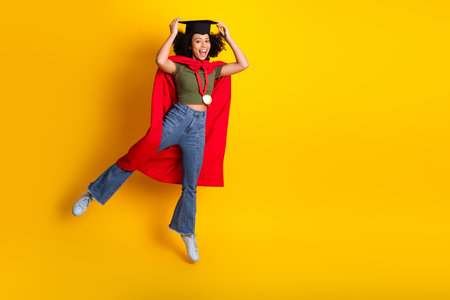 Cheerful young female graduate celebrating achievements in stylish attire against vibrant yellow backgroundの写真素材