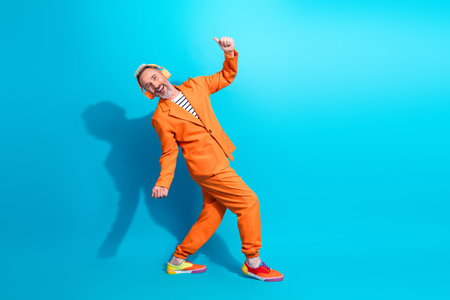 Cheerful mature man in stylish orange suit dancing joyfully against vibrant blue background, expressing happiness and confidenceの写真素材