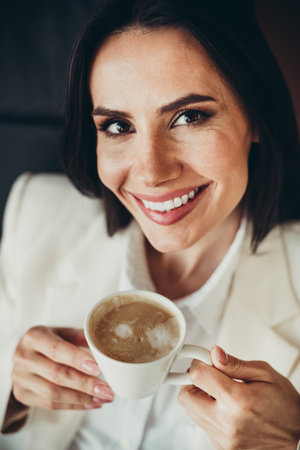 Confident businesswoman enjoying a warm coffee break while smiling bright with positivity during a professional momentの写真素材