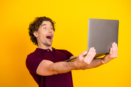 Excited young man in a polo holding a laptop against a bright yellow backgroundの写真素材