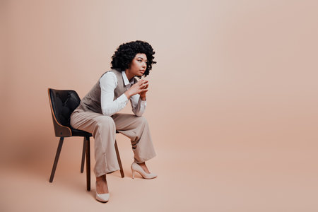 Confident businesswoman in stylish formal wear seated against a light beige background demonstrating focus and poiseの写真素材