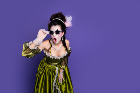 Woman in elegant green medieval costume posing on vibrant purple backgroundの写真素材