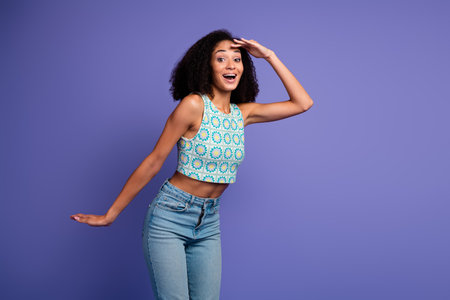 Charming young woman with afro hair in stylish summer outfit expressing happiness against purple...