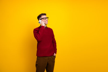 Handsome Young Man in Casual Sweater Talking on Smartphone Against Bright Yellow Background