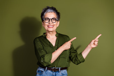 Confident senior woman smiling while gesturing with both hands against a khaki background