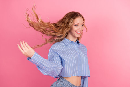 Confident young woman in stylish striped shirt and casual jeans posing joyfully against a bright pink background with energyの写真素材