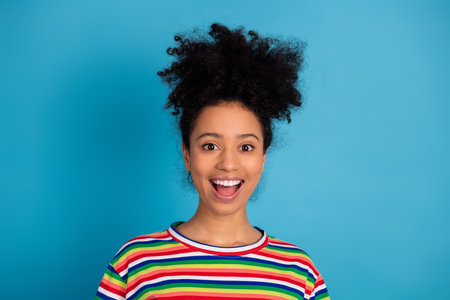 Smiling young woman in colorful striped shirt posing against turquoise background exuding happiness...