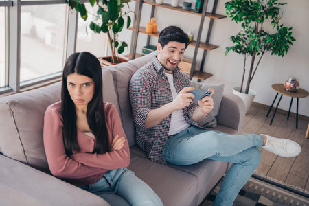 Playful moment between couple at home as man enjoys video game while woman appears indifferent on a...