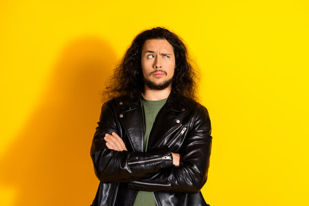 Casually dressed man with long black hair and a leather jacket looking thoughtful against a bright yellow backgroundの写真素材