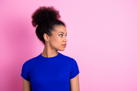 Portrait of a stylish woman with curly hair wearing a blue shirt, standing before a pink background, glancing asideの写真素材