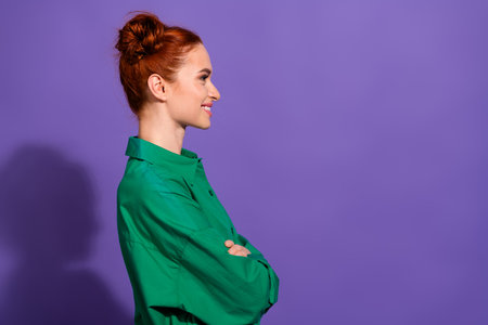 Charming young woman with red hair in a stylish green shirt against a vibrant purple background, side profileの写真素材