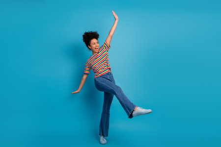 Happy young woman dancing joyfully in a vibrant casual outfit, wearing a striped t-shirt and jeans...