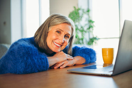 Mature woman enjoying leisure time at home, smiling in a cozy indoor setting with natural daylight...