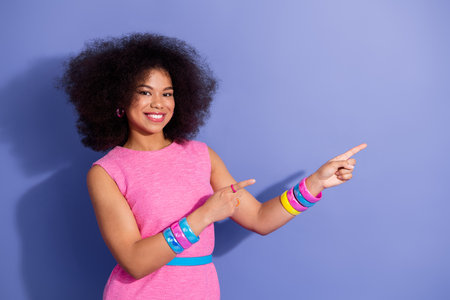 Cheerful young woman in a vibrant outfit pointing at a concept, showcasing retro style and energy...