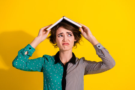 Photo of charming sad, moody woman wear trendy clothes hold book look up empty space isolated on yellow color backgroundの写真素材
