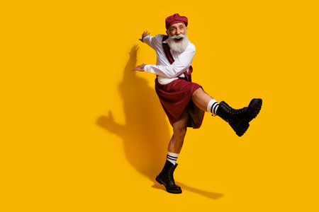 Elderly man in colorful Scottish attire joyfully dancing against a vibrant yellow background showcasing traditional cultureの写真素材