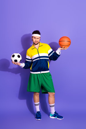 Active male athlete in vibrant retro sportswear balancing a soccer ball and basketball against a purple backgroundの写真素材