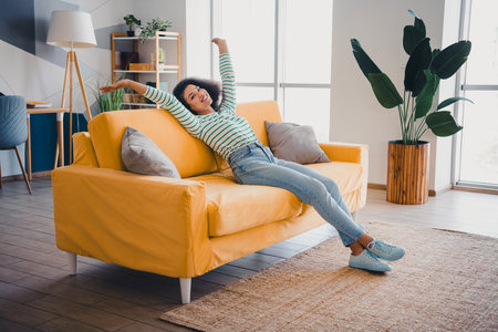 Young woman relaxing on a vibrant yellow sofa in a stylish living room filled with natural light and modern decor elementsの写真素材
