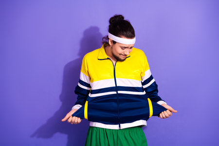 Young male athlete in colorful sportswear and headband examining his windbreaker against a vibrant purple backdropの写真素材