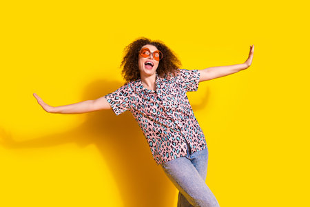 Cheerful young woman in a stylish leopard print shirt and jeans enjoying in front of a vibrant yellow studio backgroundの写真素材