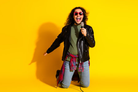 Energetic young man singing with enthusiasm in a vibrant yellow background wearing trendy clothing and styleの写真素材