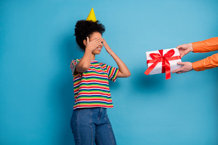 Young woman in colorful striped shirt celebrates with a surprise gift against a bright teal backgroundの写真素材